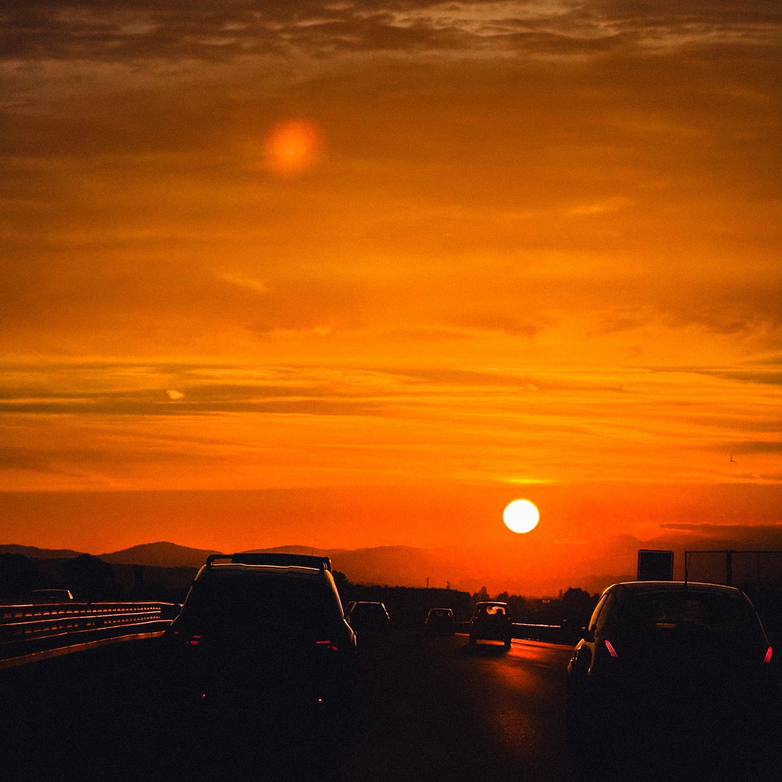 A low sun in an orange sky above road traffic.