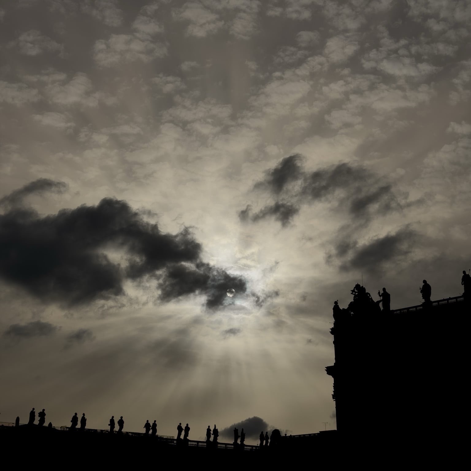Architectural outlines and statues against a light-streaked sky.