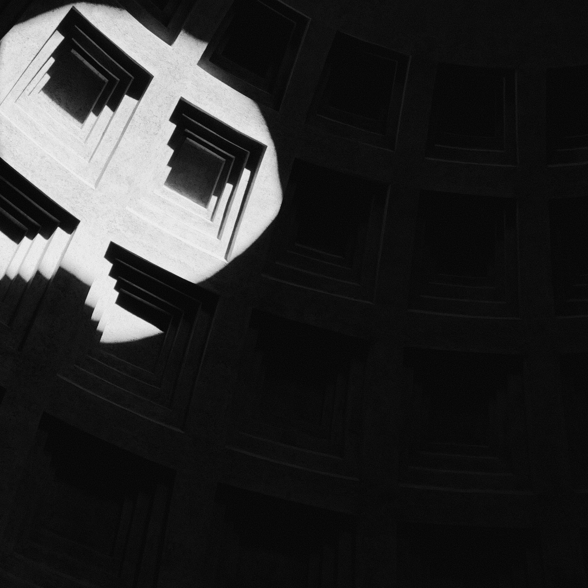 Light falling on a coffered vault, surrounded by darkness.