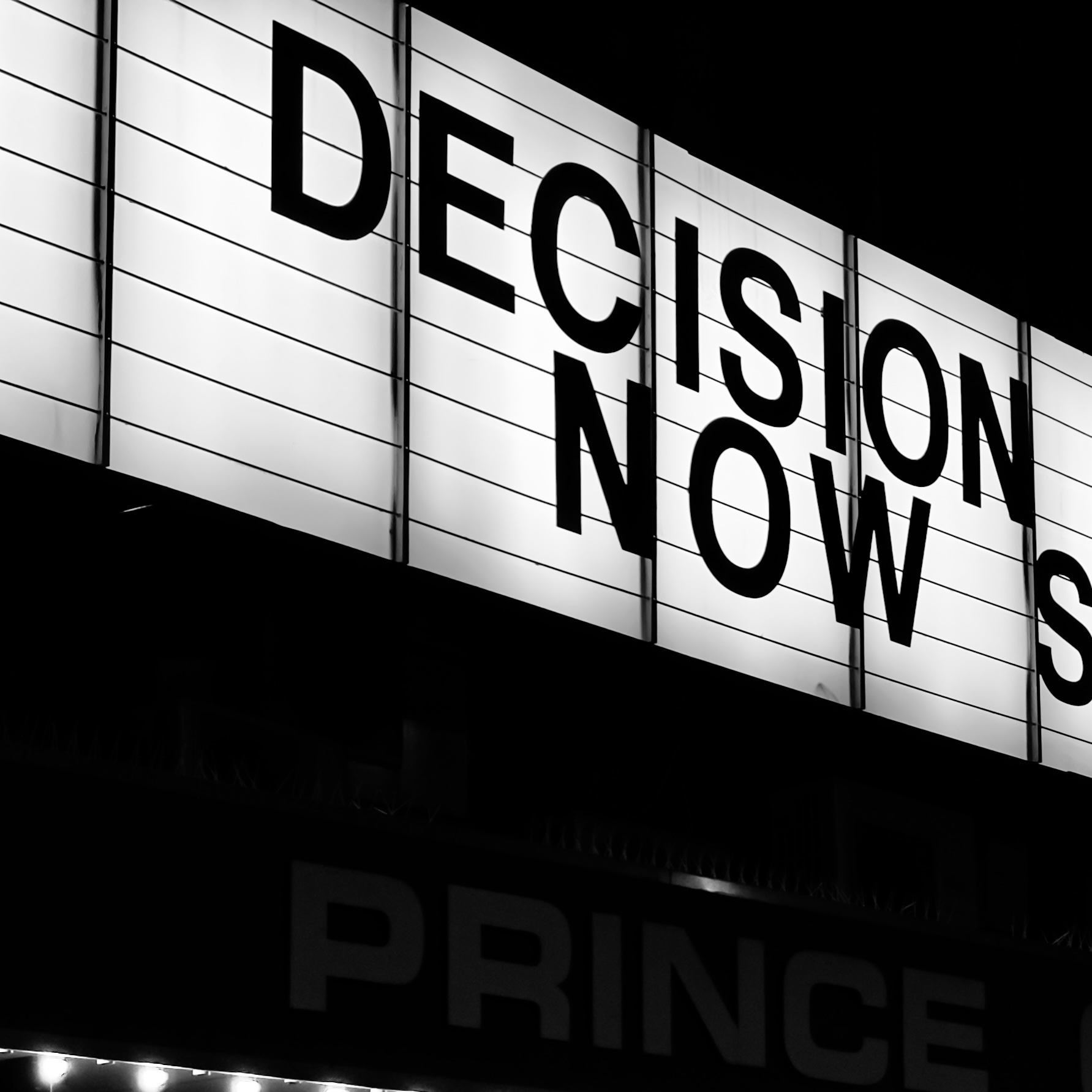 An illuminated sign reading “Decision Now”, in black and white.