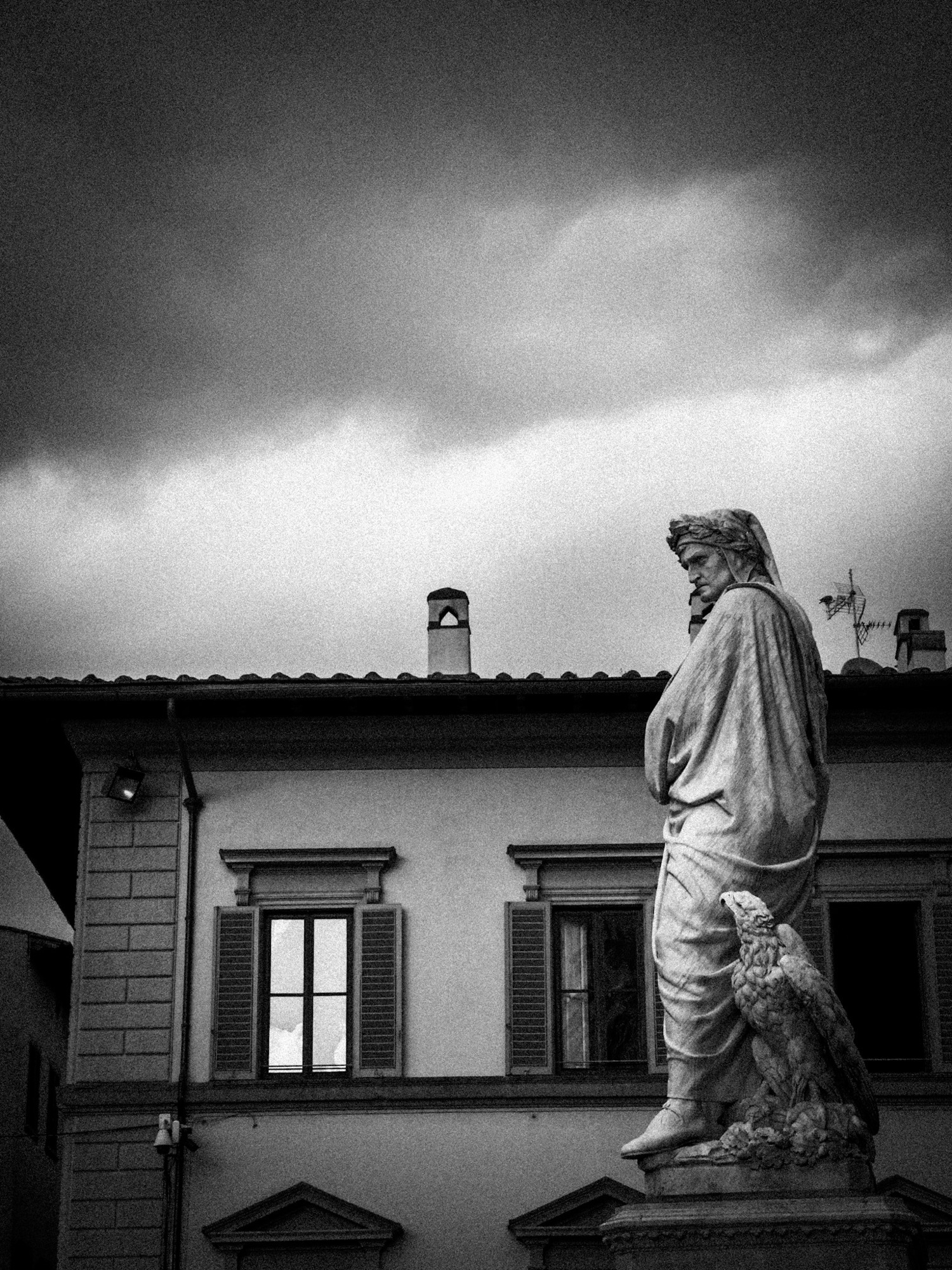 A statue in front of a building under a stormy sky, in black and white.