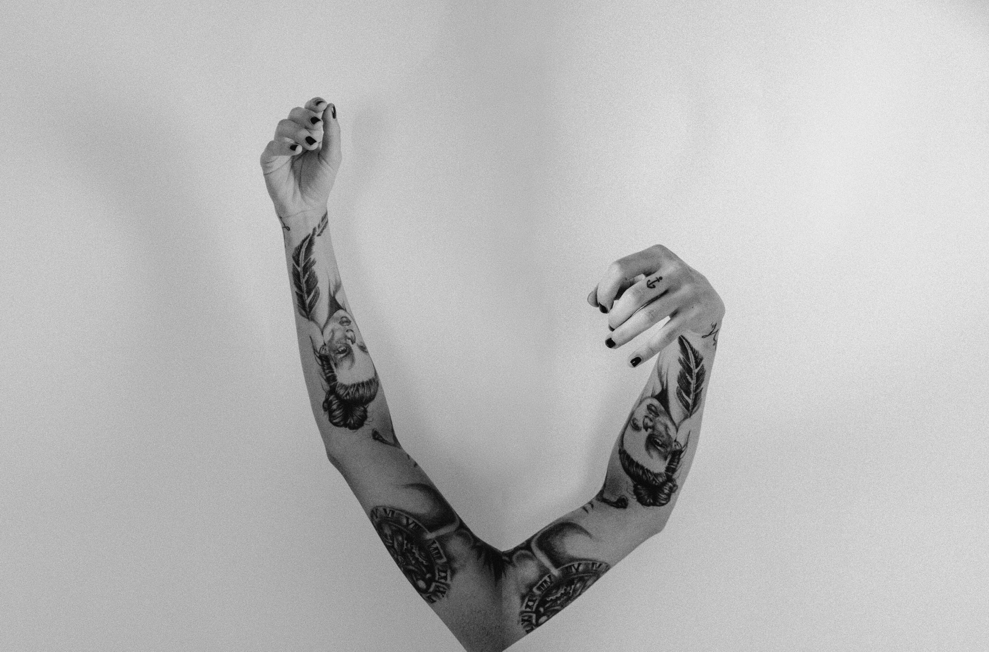 Tattooed arms raised against a pale background, in black and white.