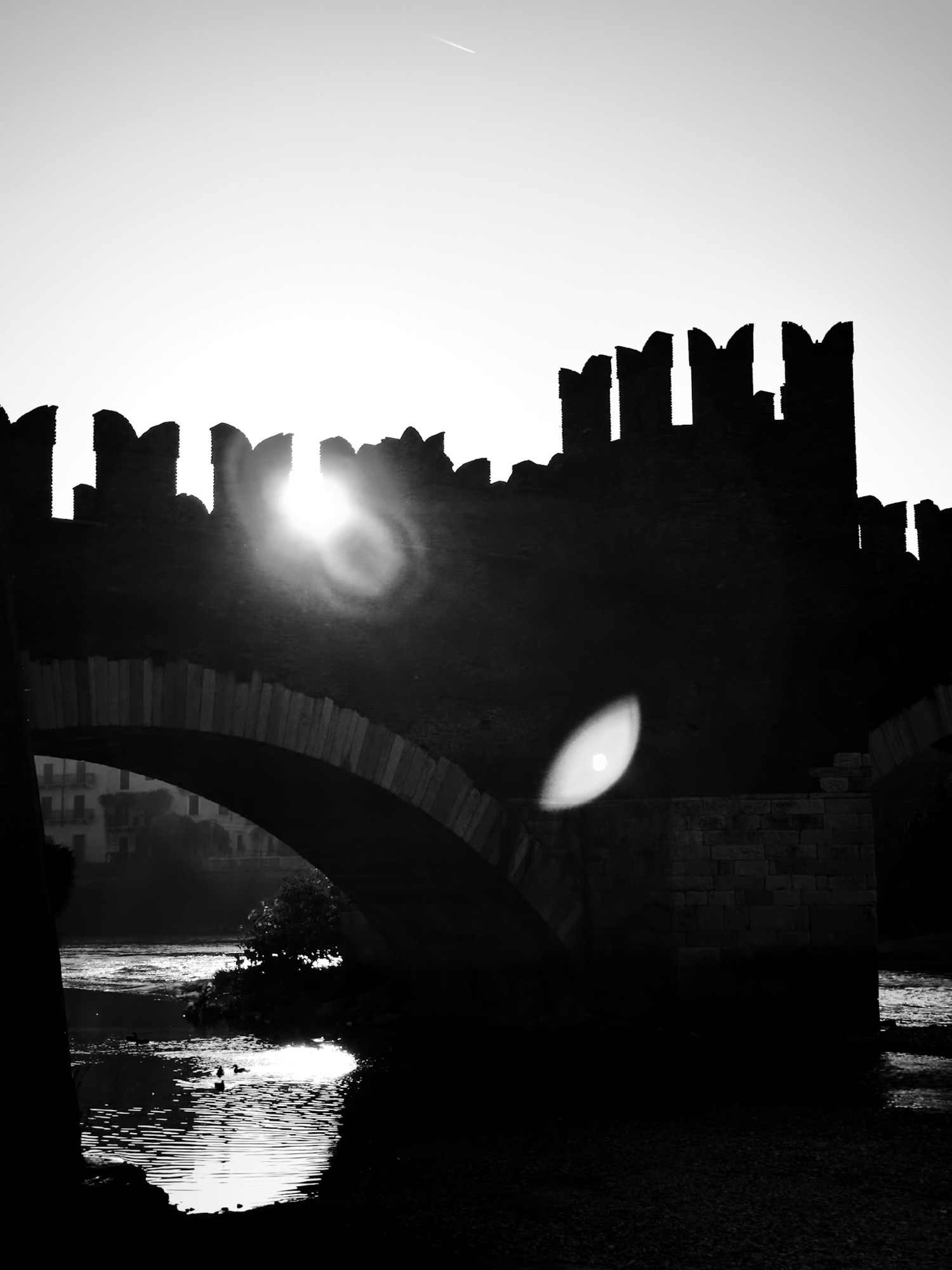 Sun through the battlements of a bridge, reflected on the water.