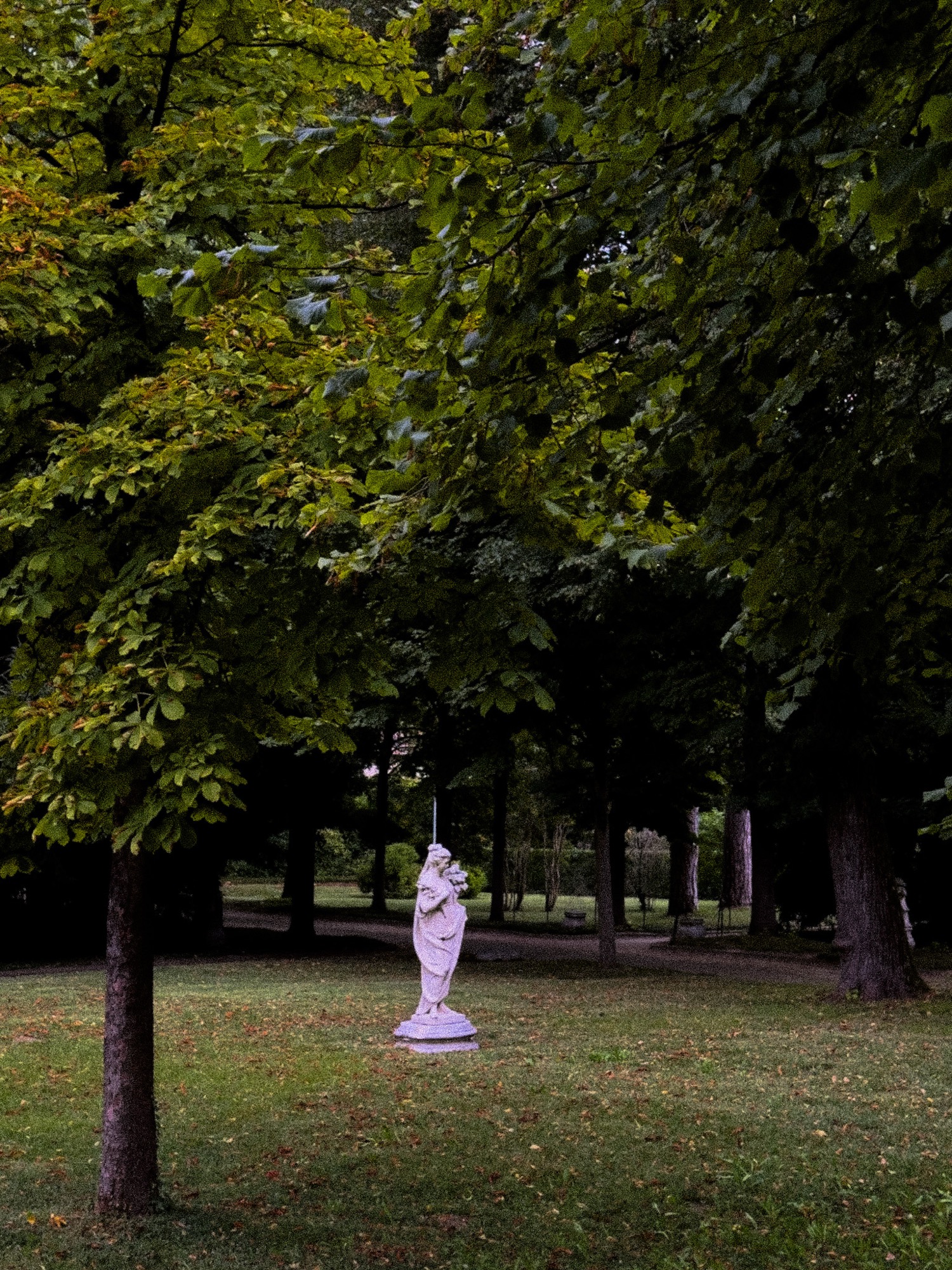 A pale statue among the green trees of a garden.