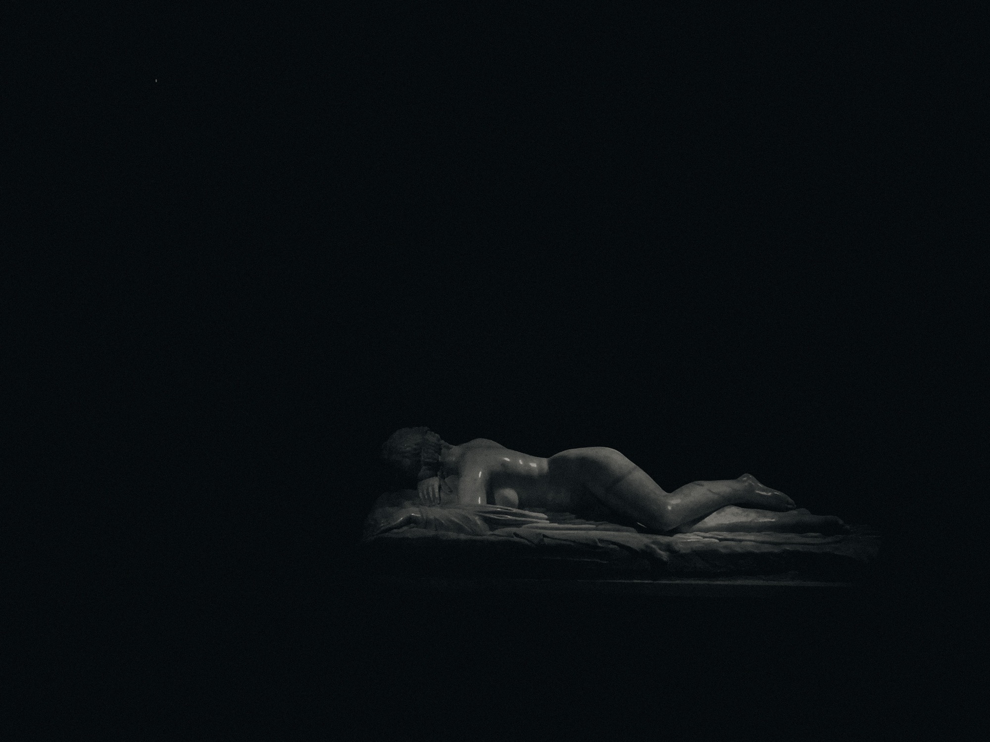 A reclining sculpted figure, isolated in darkness.