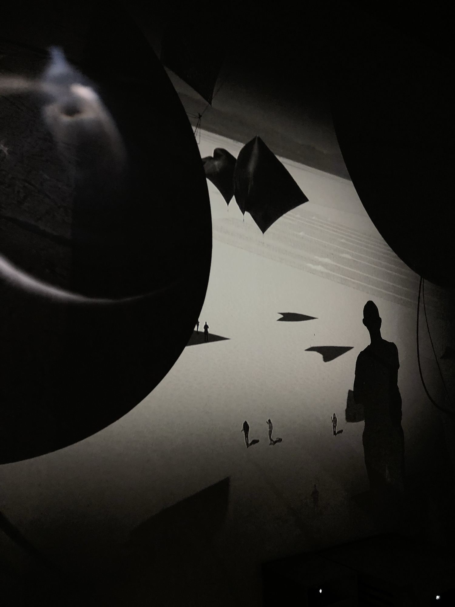 A silhouetted figure and suspended shapes in a dark exhibition space.