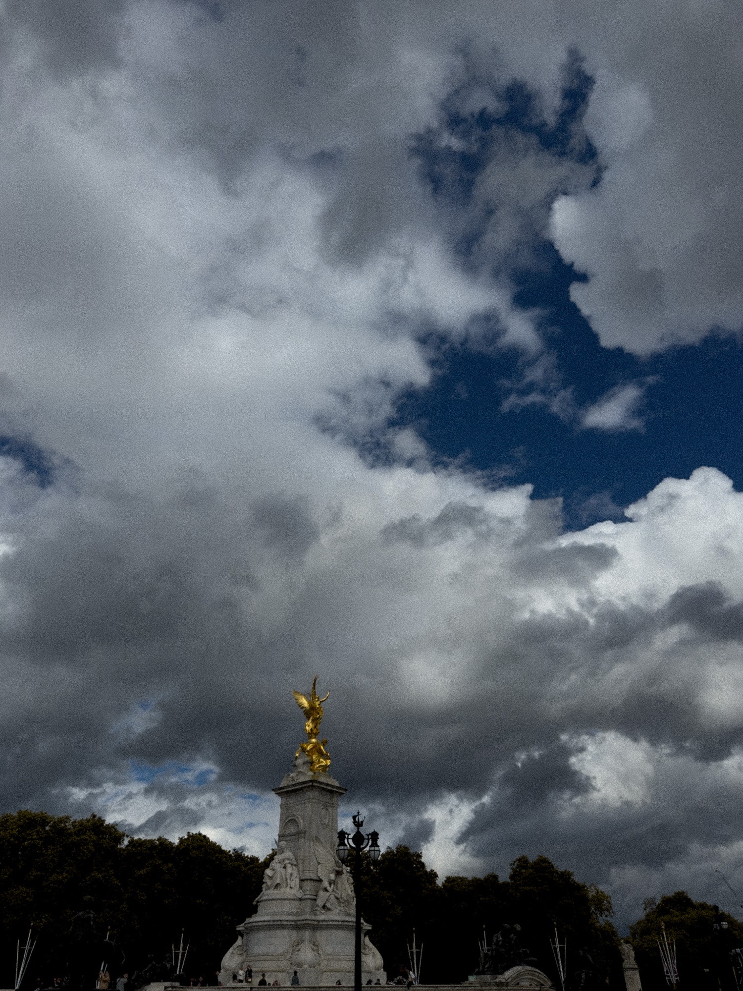 A monument topped by a golden figure beneath towering clouds.
