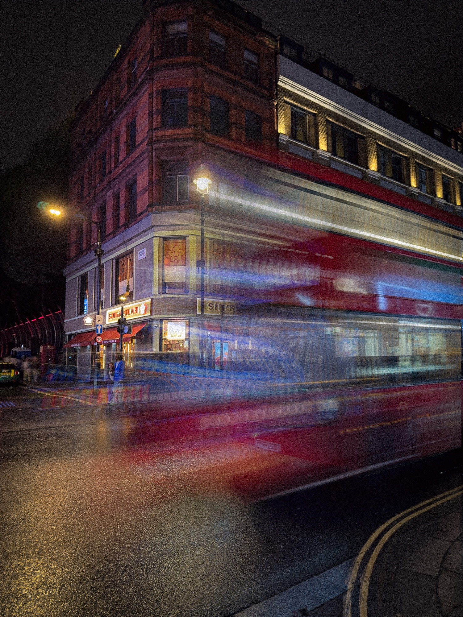 Light trails of a red bus moving along a street at night.