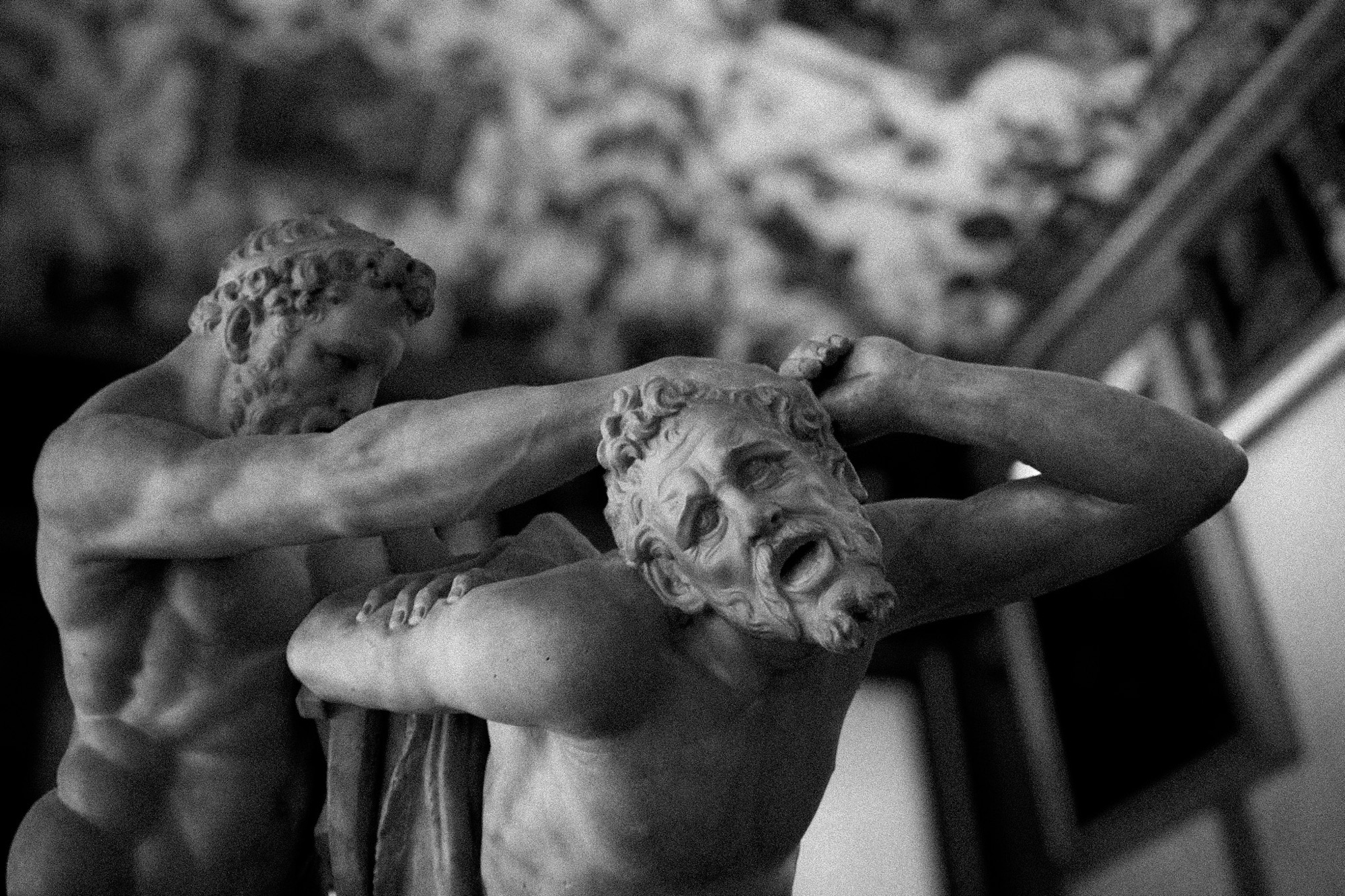 Intertwined arms and faces of a sculptural group, in black and white.