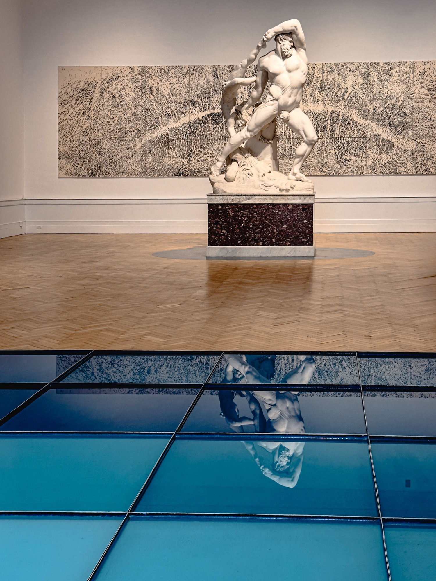 A sculpture in a gallery, reflected in a blue surface.