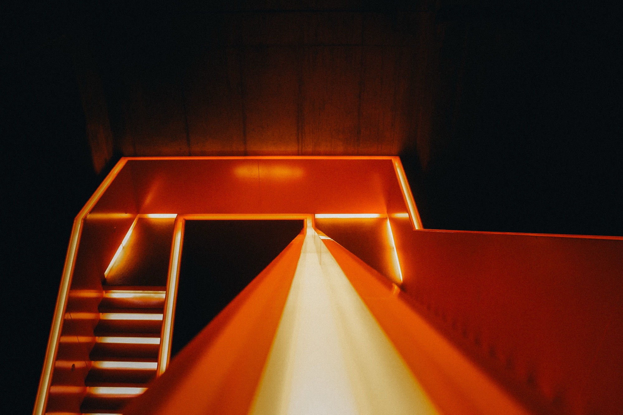 Orange architectural lines and a lit staircase in the dark.